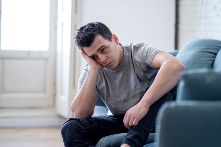 A young man with his head in his hand sitting on a couch.