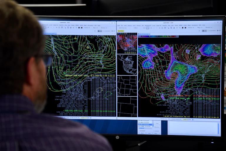 A man looks at a computer screen displaying satellite images.