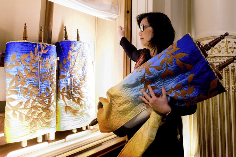 A woman removes a Torah scroll from the ark, a cabinet that houses scrolls of the Hebrew Bible.