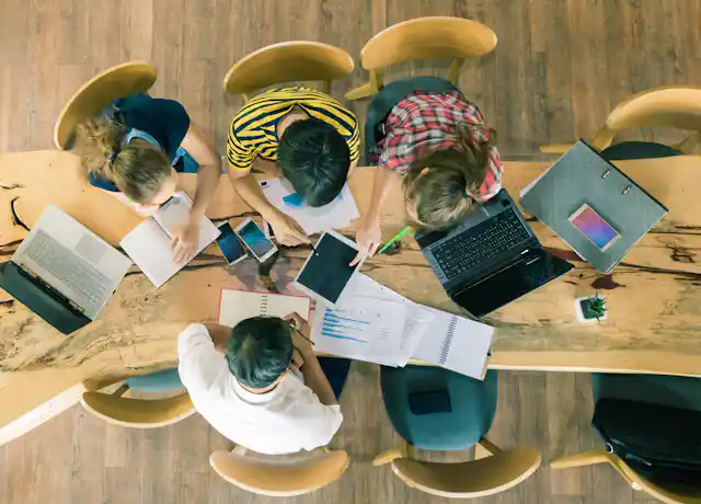 A bunch of people at a big table working on laptops and ipads