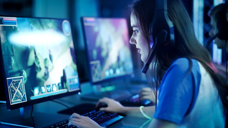 A girl sits behind a computer screen playing a video game