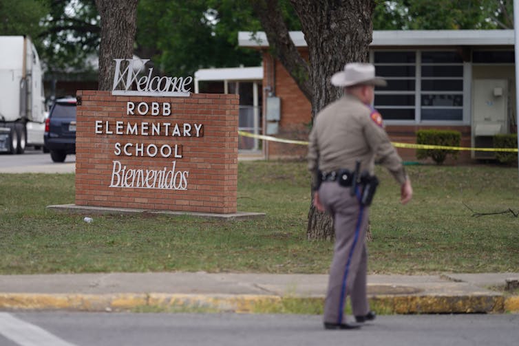 A uniformed officer walks past a sign saying 'Welcome Robb Elementary School Bienvenidos'