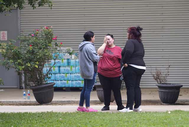 Three women talking outside a building, one of them crying.