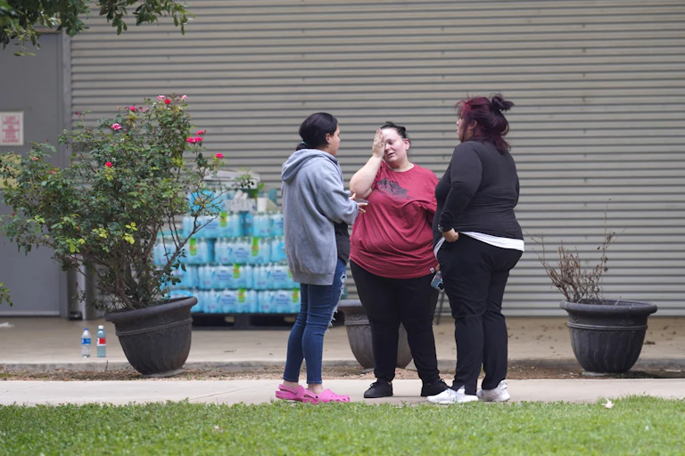 Three women talking outside a building, one of them crying.