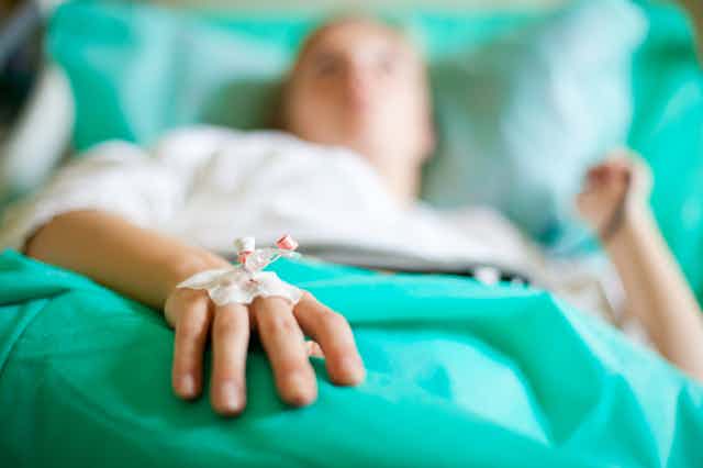 Person lying on hospital bed with medicine dripping into hand