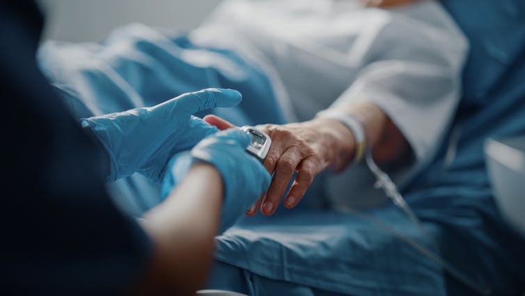 Sick elderly patient in hospital bed, nurse wearing gloves holding fingertips