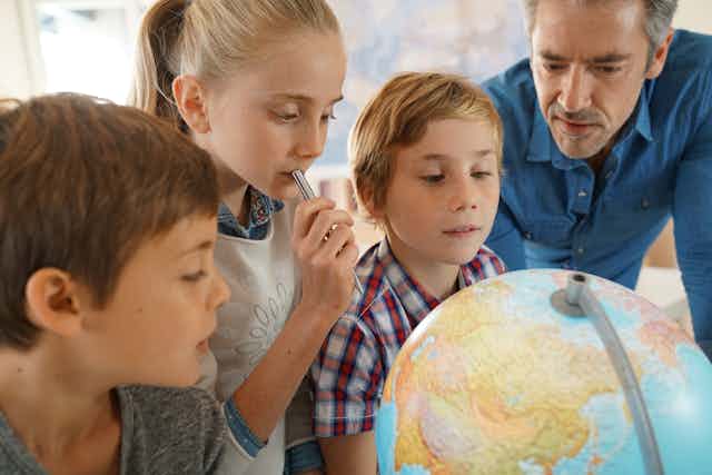 Three children and teacher looking at globe of world