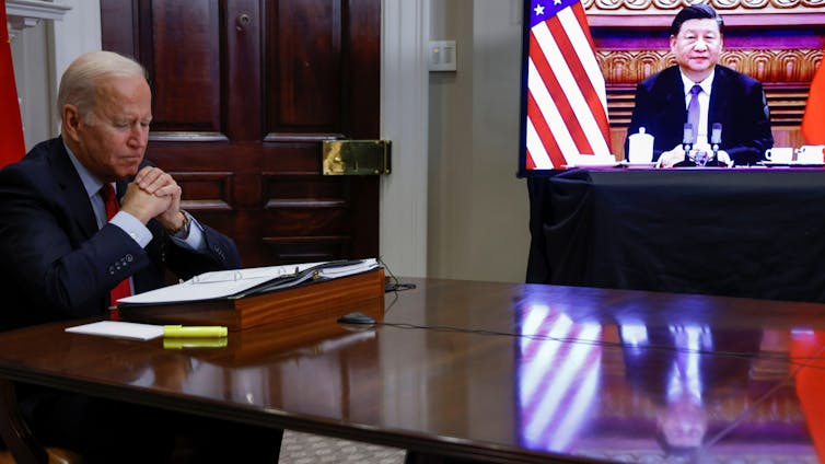 US president Joe Biden in a suit, with President Xi of China on a screen.