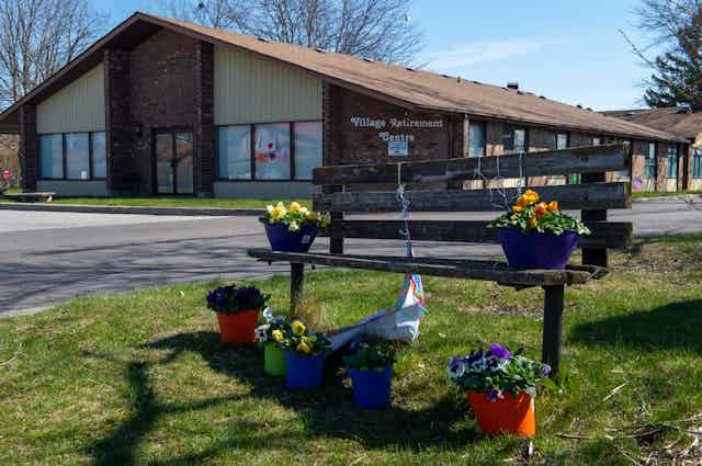 A bench with pots of pansies is seen in front of a long-term care home.
