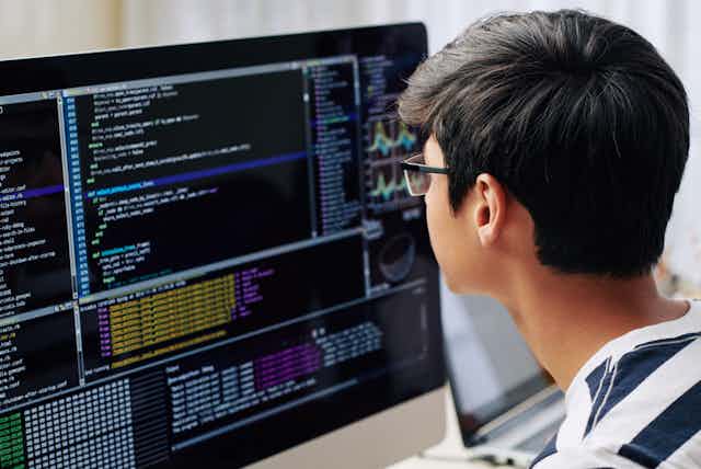 Un adolescent intelligent en lunettes vérifiant le code de programmation sur l'écran de l'ordinateur lorsqu'il est assis à son bureau