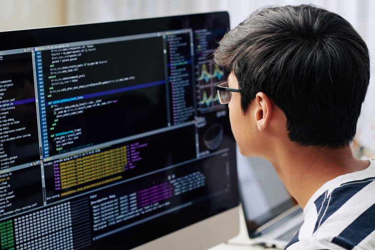 Un adolescent intelligent en lunettes vérifiant le code de programmation sur l'écran de l'ordinateur lorsqu'il est assis à son bureau