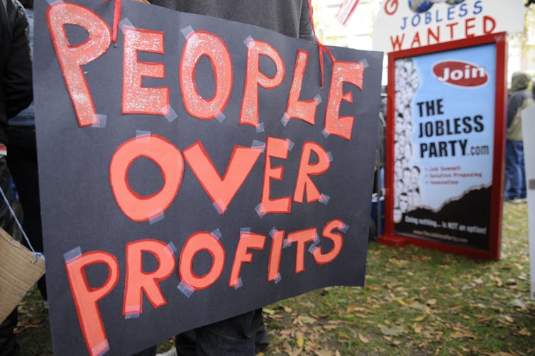 A handmade black sign with red lettering that reads 'People over profits'.