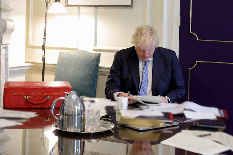 Boris Johnson sitting at a table reading the Sue Gray report.