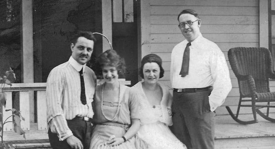 A photograph of a two smiling white couples standing next to each other near a front porch.