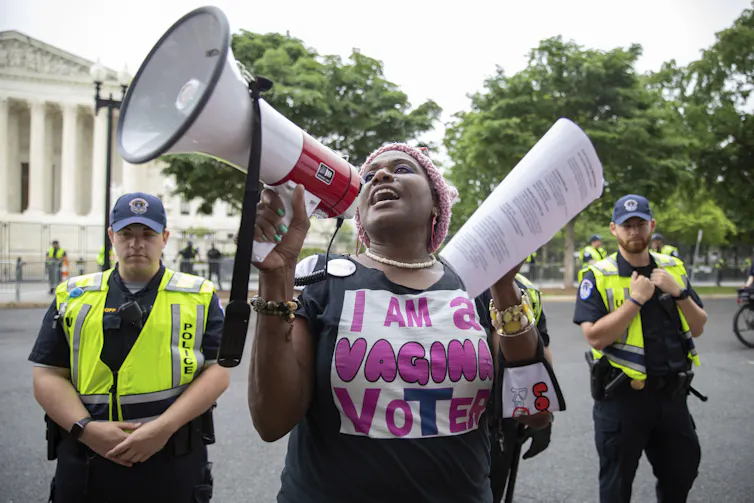 A woman with a megaphone wears a shirt that says 'i am a vagina voter'