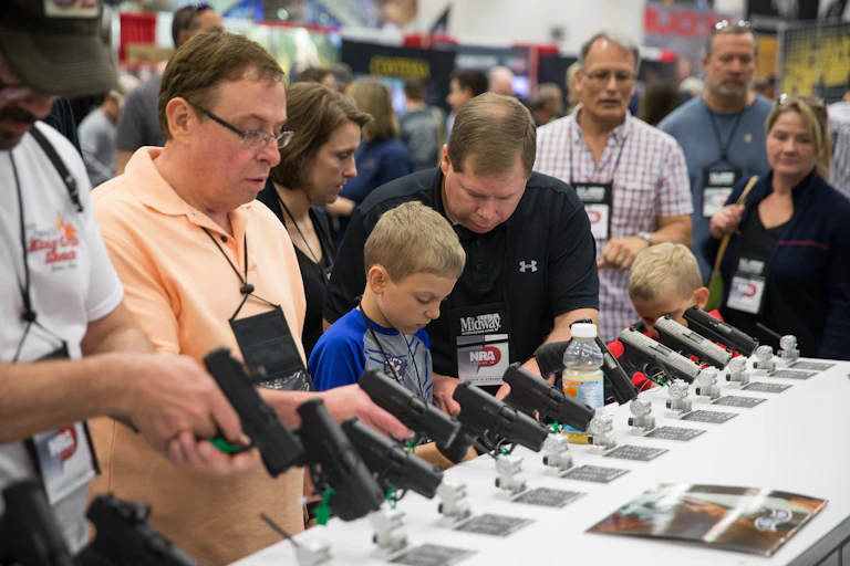 White people examine guns at a display case.