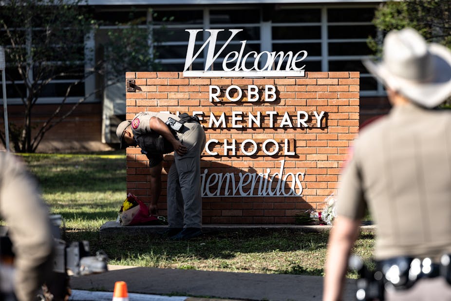 A Texas state trooper lays down flowers at the base of a sign bearing the words, Welcome and Bienvenidos, Robb Elementary School, where 21 people were killed in a mass shooting on May 24, 2022.