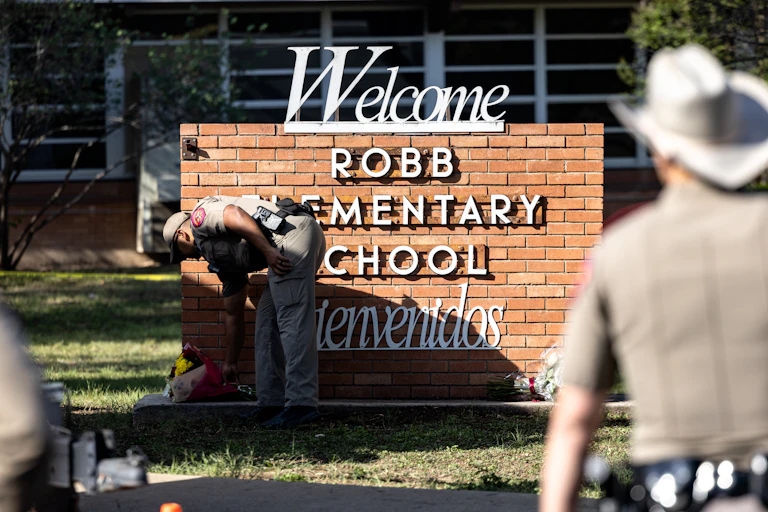 A Texas state trooper lays down flowers at the base of a sign bearing the words, Welcome and Bienvenidos, Robb Elementary School, where 21 people were killed in a mass shooting on May 24, 2022.