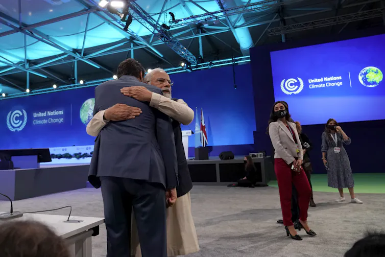Two men embrace with blue United Nations climate summit signs behind them.
