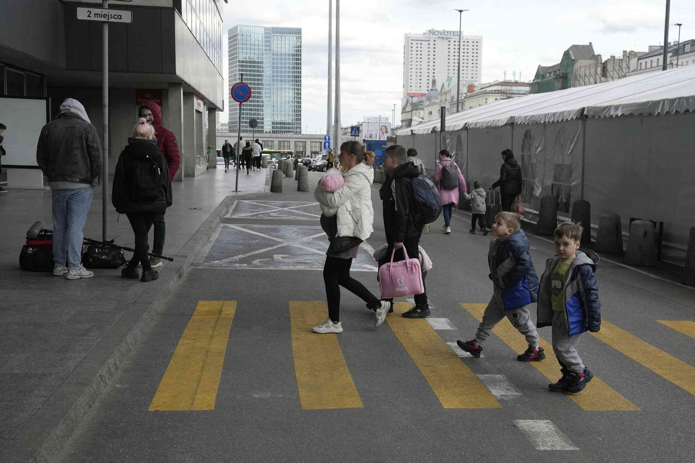 A woman crosses a crosswalk followed by two children outside of a train station.