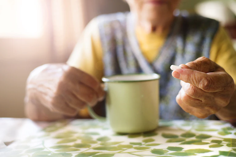 Older woman sitting at her table takes a tablet.