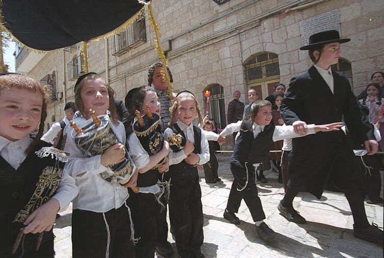 Young boys walk under a canopy as they clutch Torah scrolls.