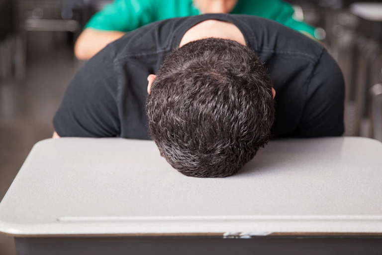 Boy sitting at desk puts his head on the table