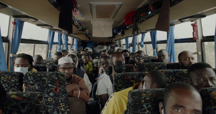 A crowded bus in transit, people staring ahead, out the windows.