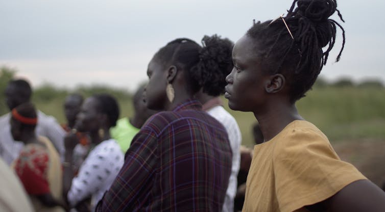 Two women in the foreground standing with a small group of women, all looking back at something.