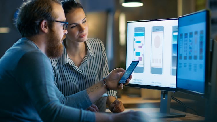 A man and women work on developing a mobile app together looking at a computer monitor