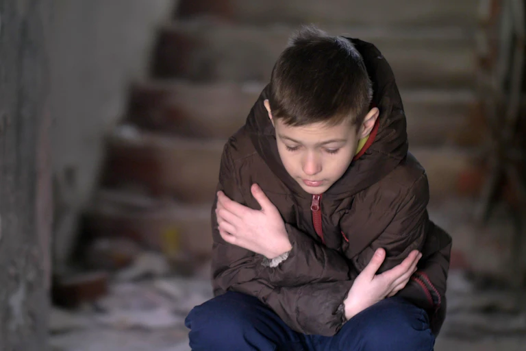 Child in winter coat sits on stairs shivering.