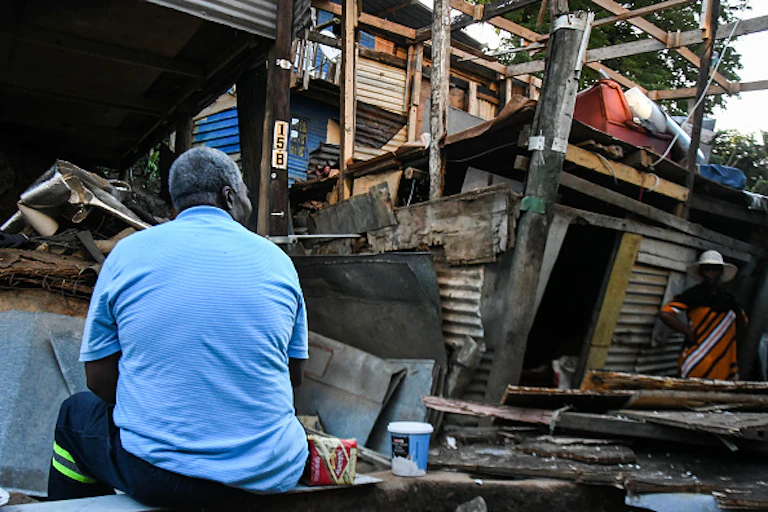 Man sitting in front of ruins of his shack