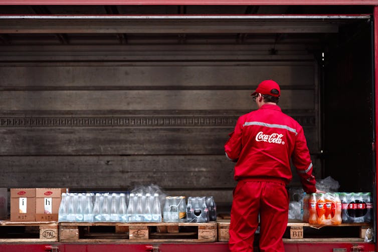 A person in Coca Cola uniform stands in front of drinks crates on a truck