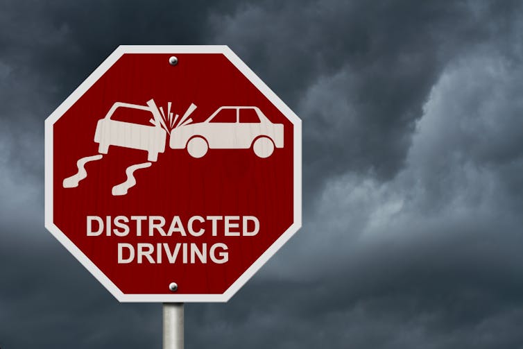 a red road sign showing a graphic of a car crash with the words DISTRACTED DRIVING