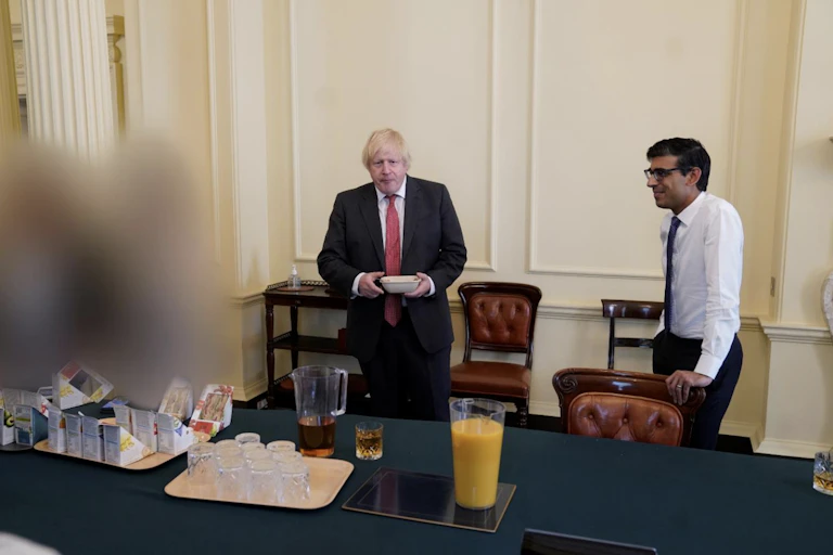 Boris Johnson and Rishi Sunak standing in front of a table of sandwiches and drinks in a photo taken from the Sue Gray report.