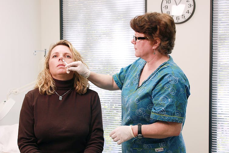 A nurse inserting an eyedropper into a woman's nose.