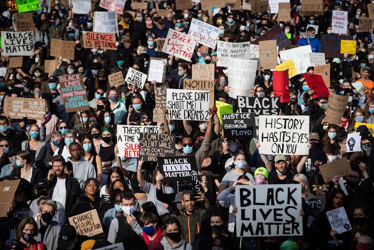 A large crowd holds signs, many read: 'Black Lives Matter.'