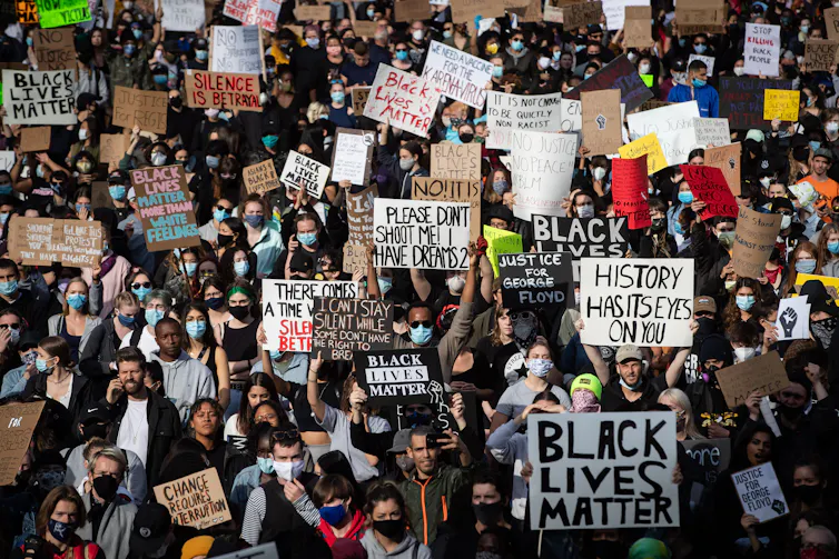 A large crowd holds signs, many read: 'Black Lives Matter.'