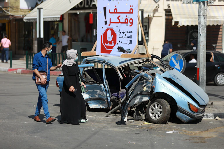 Two people walk past a mangled car, staring at the wreck
