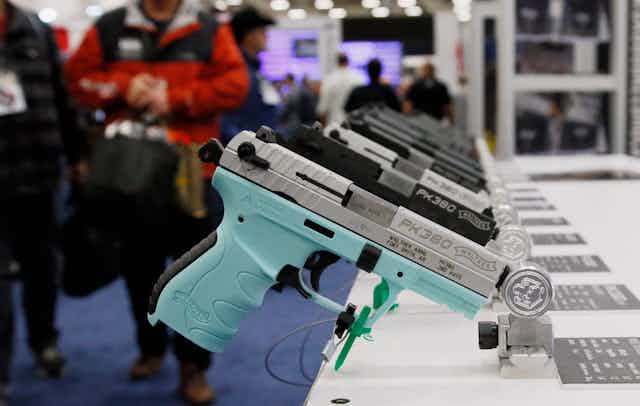 A handgun with a blue grip is on display in a line of other handguns on a table at a gun expo