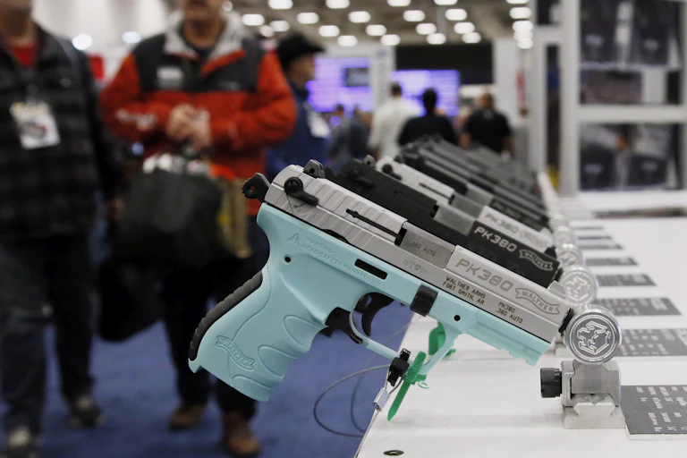 A handgun with a blue grip is on display in a line of other handguns on a table at a gun expo
