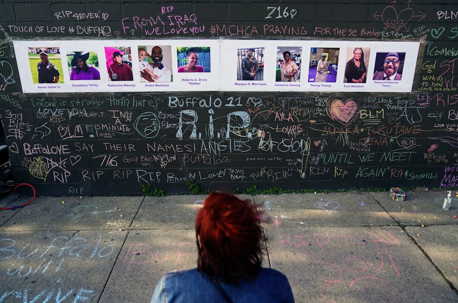 A person sits looking at a makeshift display to victims killed in a mass shooting.