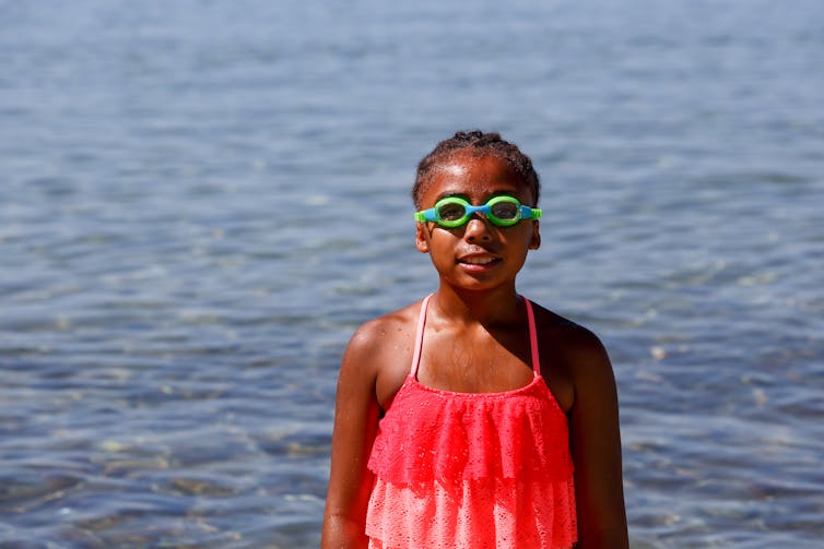 A girl in a swimsuit and swimming goggles in front of a body of water