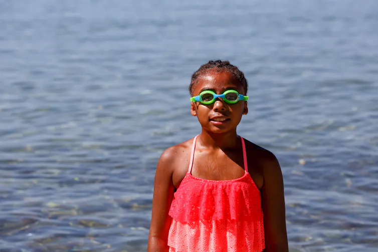 A girl in a swimsuit and swimming goggles in front of a body of water