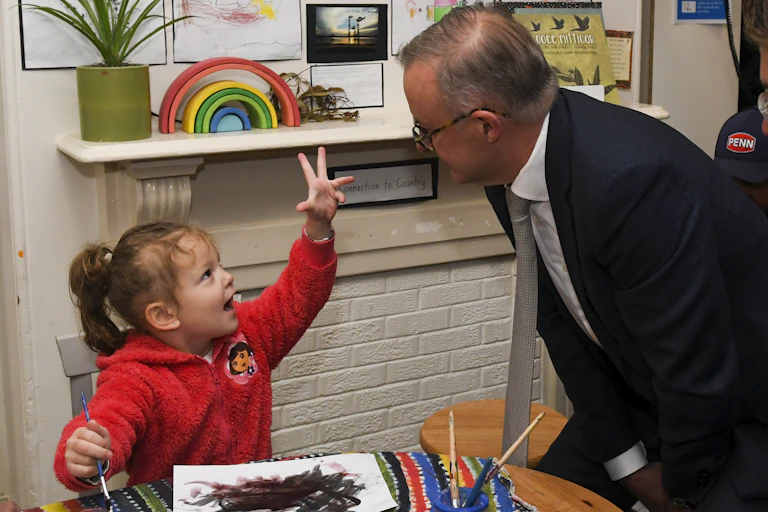 Young child raises hand as she explains what's she doing to a man in a suit