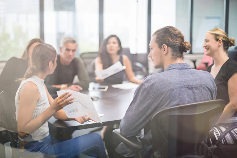 People sit together in a meeting. A First Nations person presents a paper to the group.