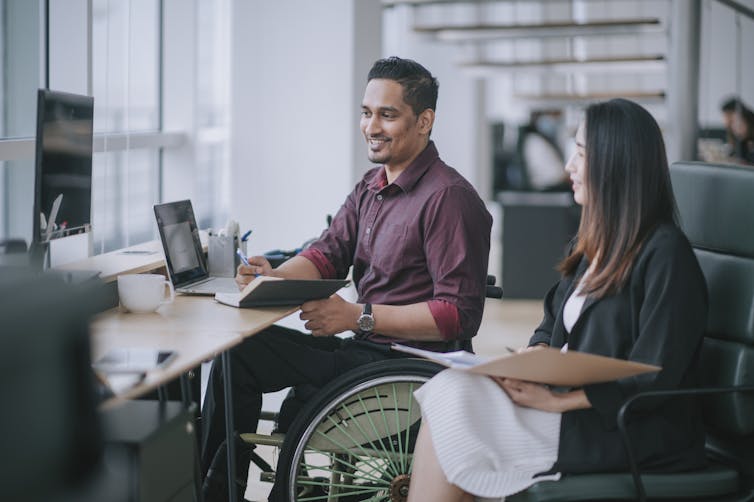 Man in wheelchair at desk talks to female colleague