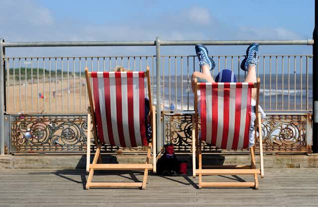 Rear view of couple relaxing on deck chairs.