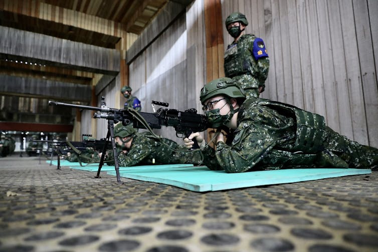 Taiwanese riflemen practise target shooting from a prone position supervised by an instructor in the background.