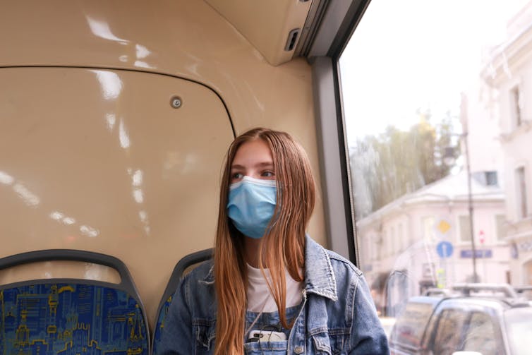 A young woman on a bus wearing a mask.